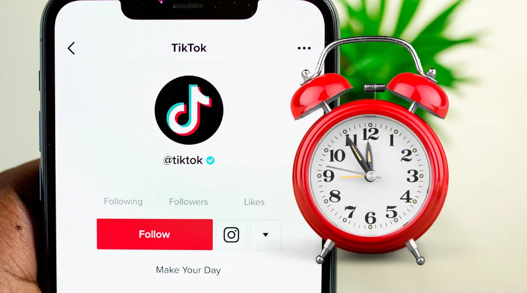 A closeup of a smartphone with TikTok's own TikTok profile open with a old timey red clock floating next to it