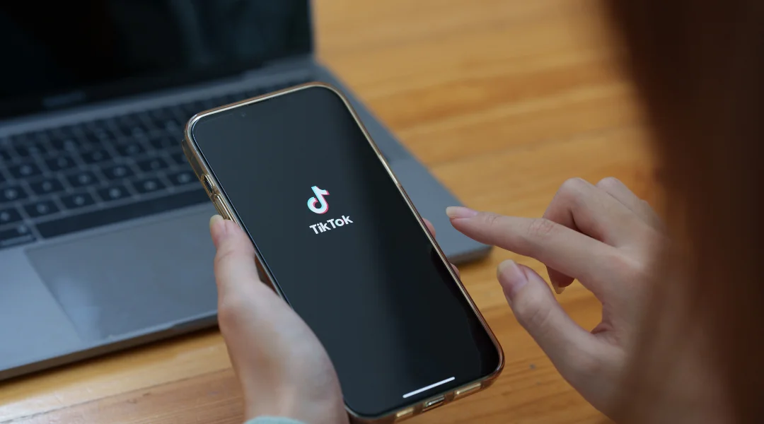 A woman holding a smartphone with the TikTok logo appearing on the screen