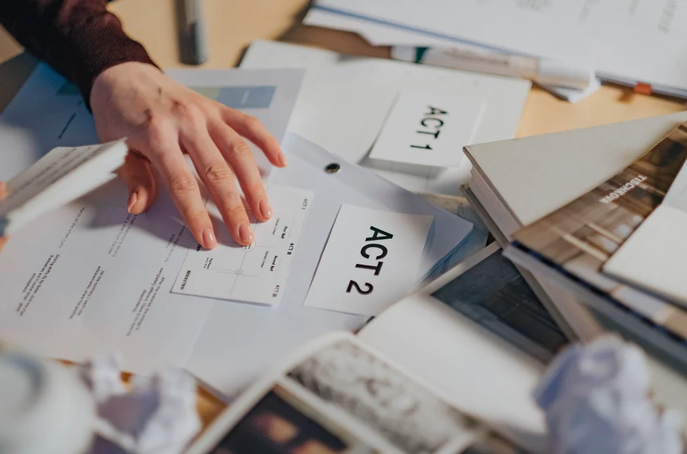 A person outlining a plot. Several flashcards and papers are scattered on the table. The flashcards say 'Act 1' and 'Act 2'.