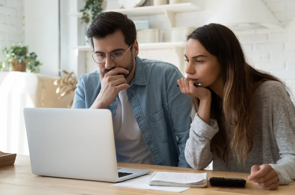 Two people sitting in front of the desk looking at the laptop. They are resting their chin on their right hands.