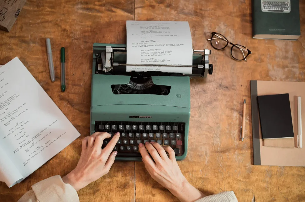 A person typing a script on a green typewriter