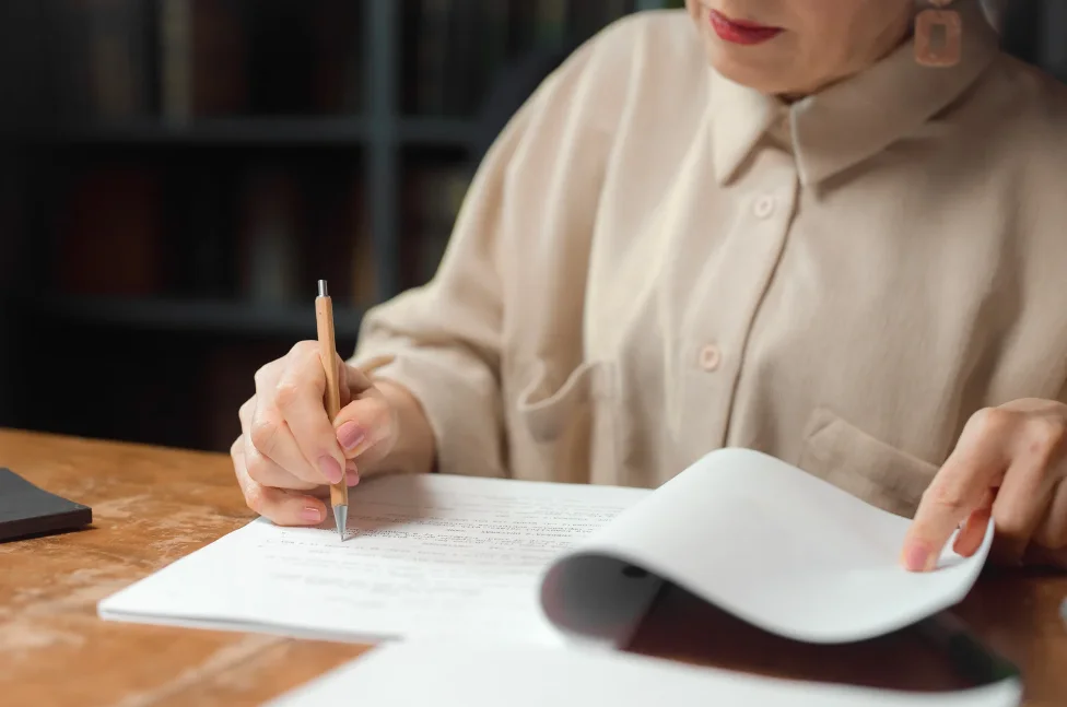 A woman revising a plot. She is holding a pen writing something on a paper.