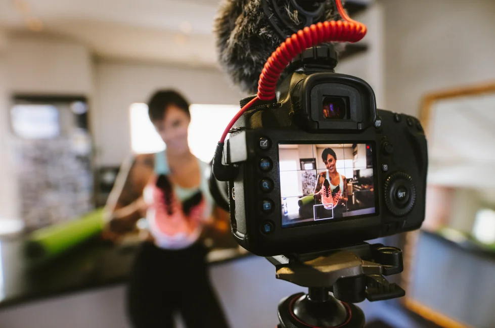 A woman filming a video of herself. She is holding her pink shoes.