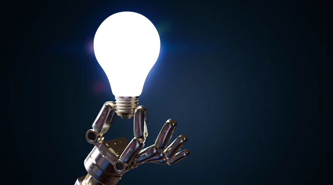 A robot hand holding a turned on white lightbulb in front of a dark blue background