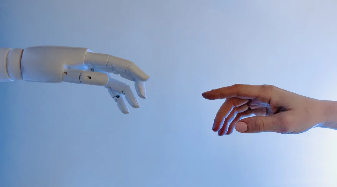 A white robot hand reaching for a woman's hand