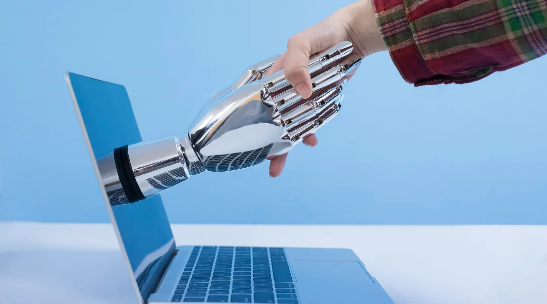 A man shaking hands with a shiny robot hand coming out of a mac book
