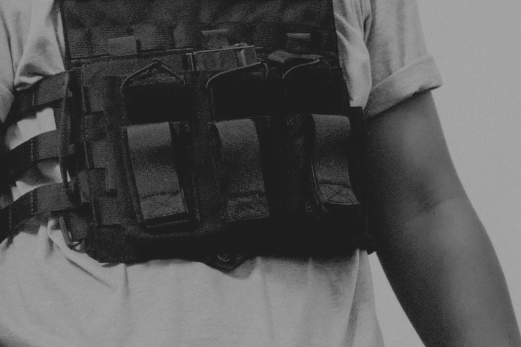 Person wearing a tactical vest with multiple pouches over a rolled-up short sleeve shirt.