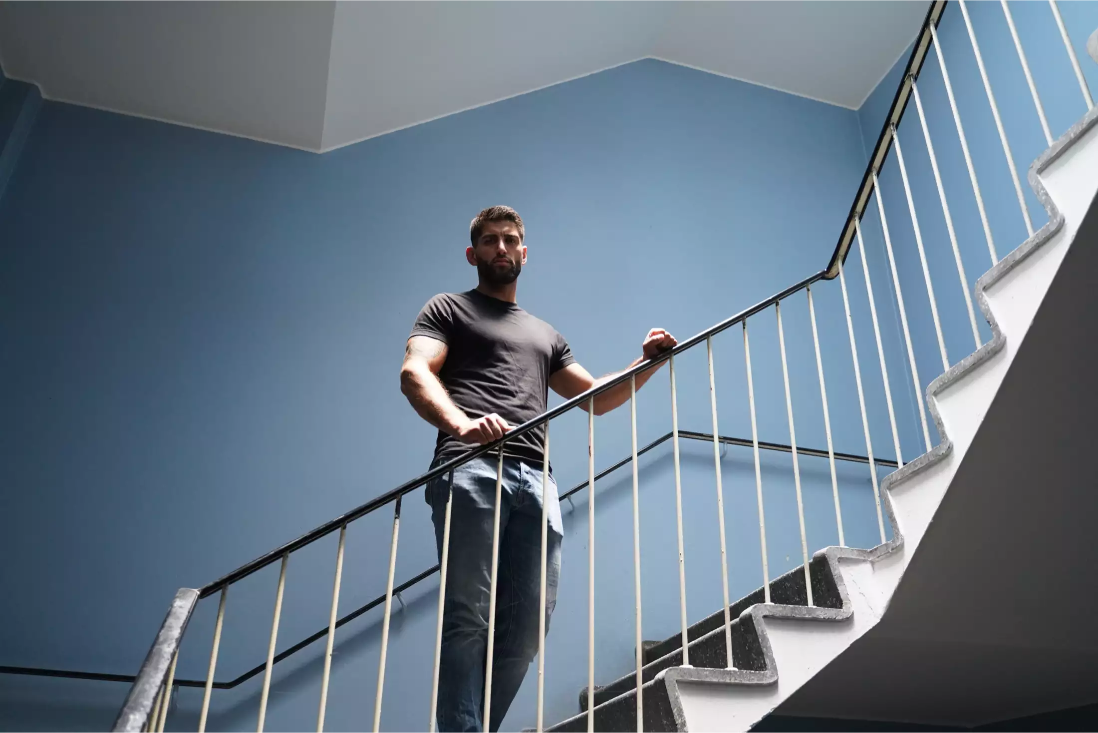 Mand i sort t-shirt og jeans står på en trappe med blå væg bagved.