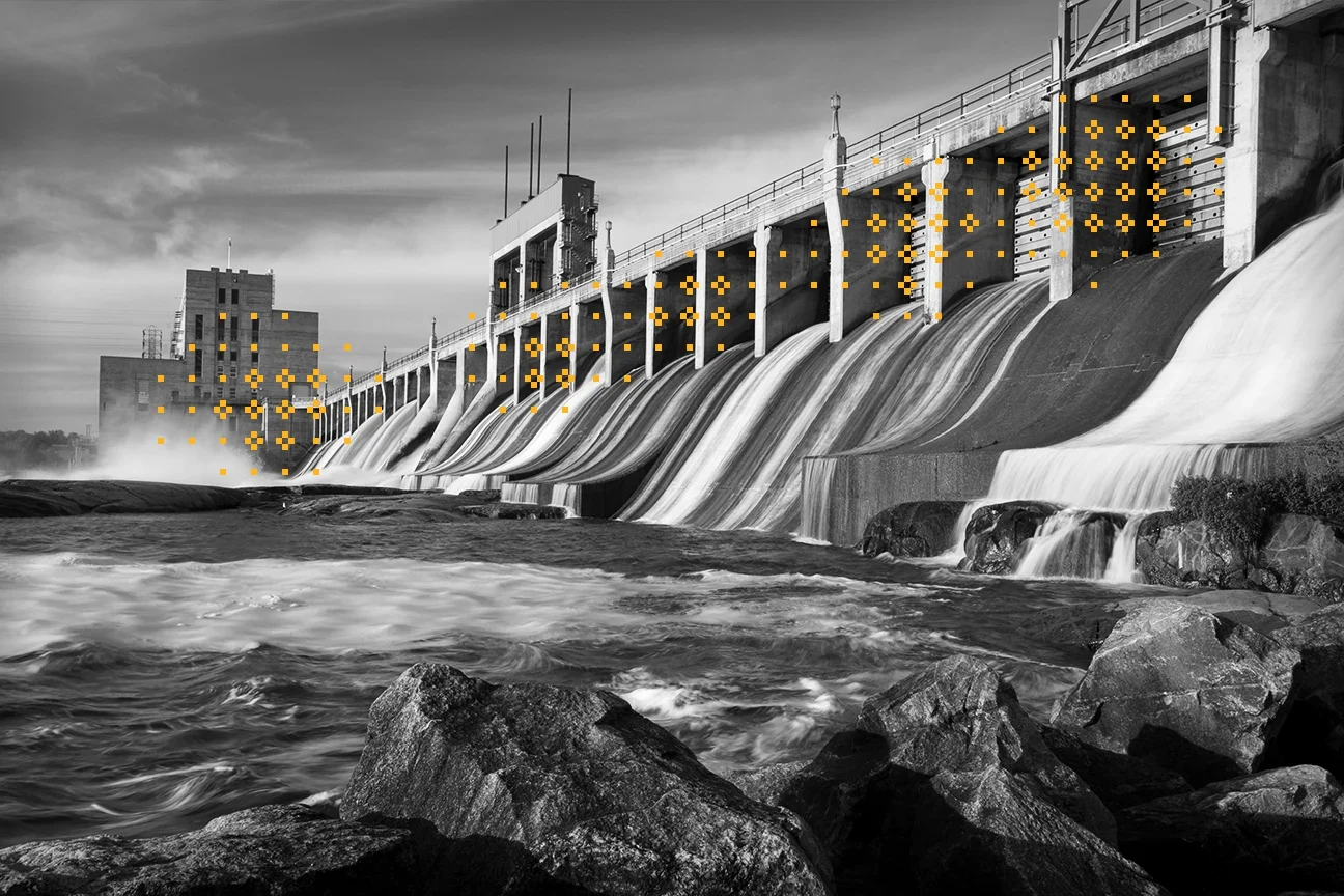 water rushing from a hydroelectric dam surrounded by large rocks with yellow decorative glyphs along the dam