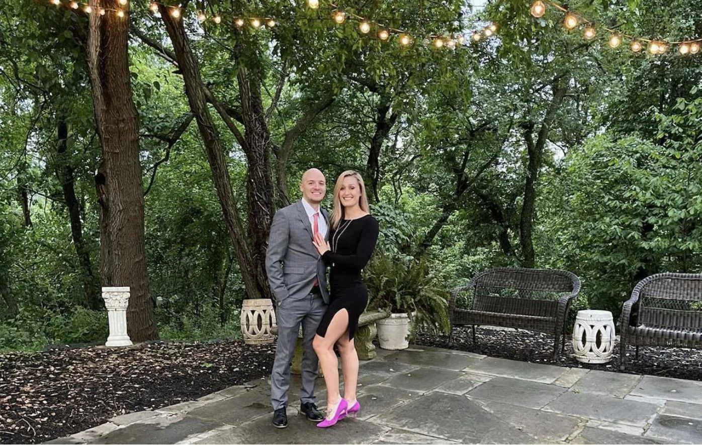 Married couple standing nearby trees underneath bright string lights