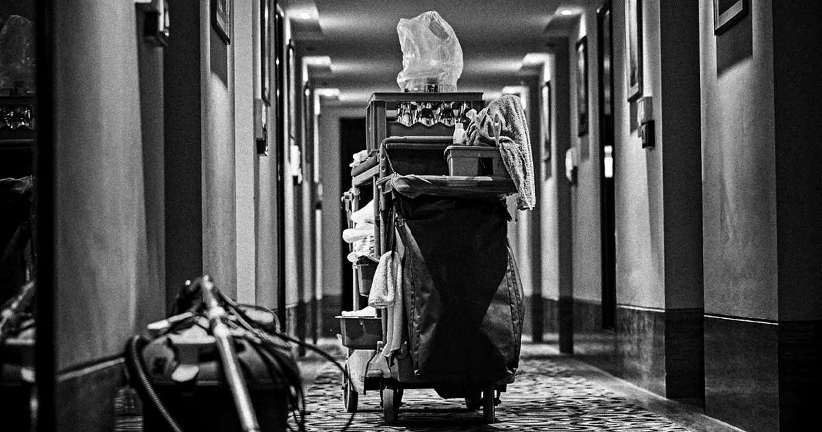 Hotel hallway housekeeping push cart with a vacuum on the floor in the foreground.