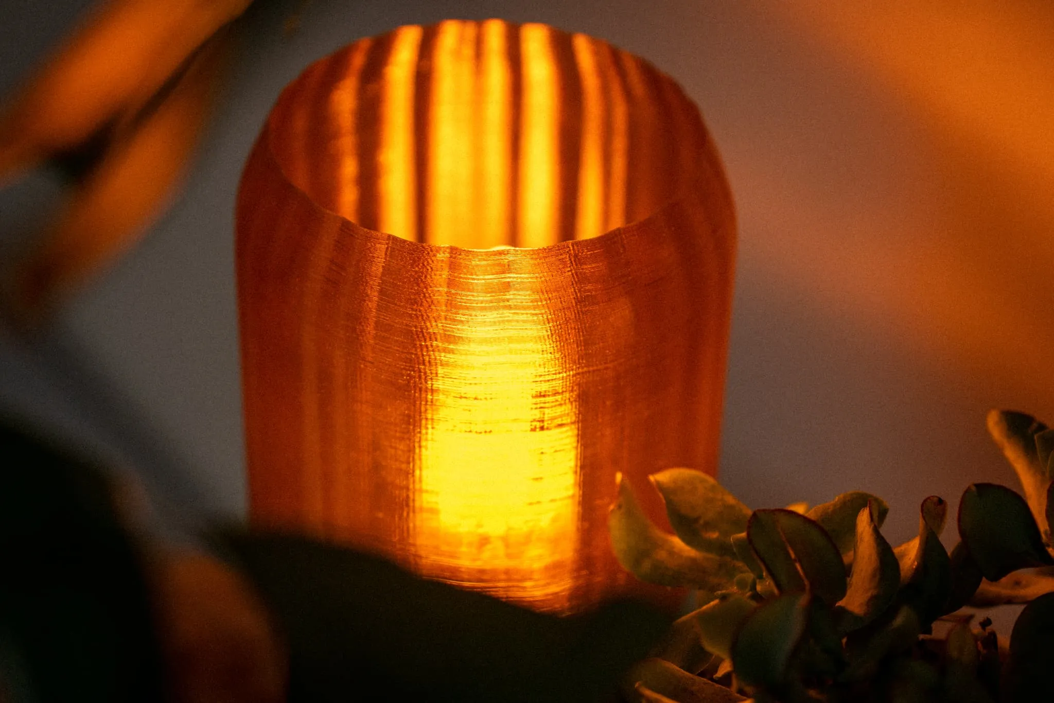 Lumină caldă portocalie care strălucește printr-un obiect cilindric texturat, cu frunze verzi la margine.