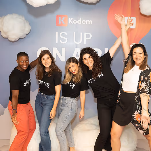 Five smiling young women posing energetically in front of a backdrop with Kodem branding and fluffy cloud decorations.