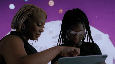 Two women looking at a tablet together, one pointing at the screen, with a purple background featuring planets.