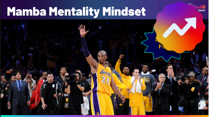 Kobe Bryant waves to the crowd on a basketball court wearing a Lakers uniform with teammates and coaches applauding behind him.