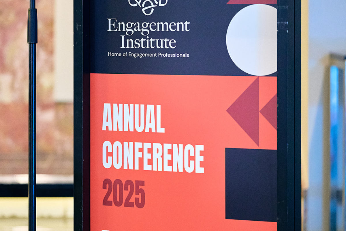 A close-up photo of a sign for the Engagement Institute’s Annual Conference 2025. The design features bold red, white, and dark blue geometric shapes with the tagline “Home of Engagement Professionals.”