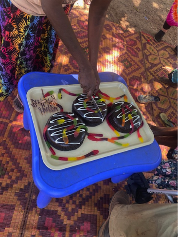Someone cutting into one of three round chocolate cakes covered in gummy snakes. The cakes are served on a white tray, which is on a small blue table.