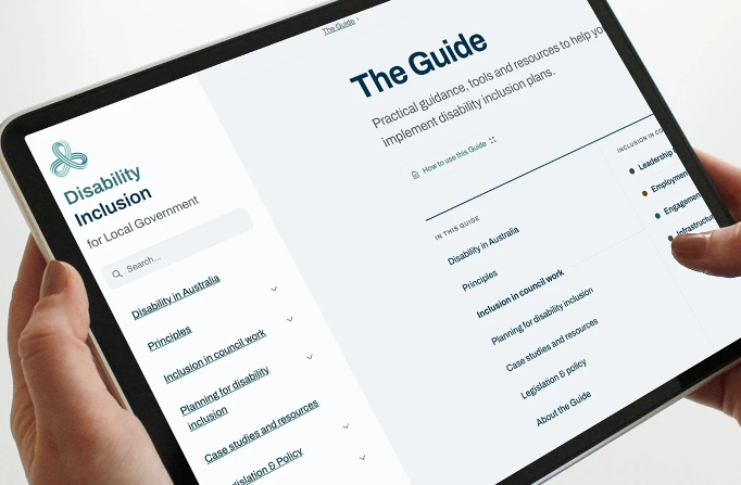 Hands holding a tablet showing a website called "Disability Inclusion for Local Government" open to a page titled "The Guide".