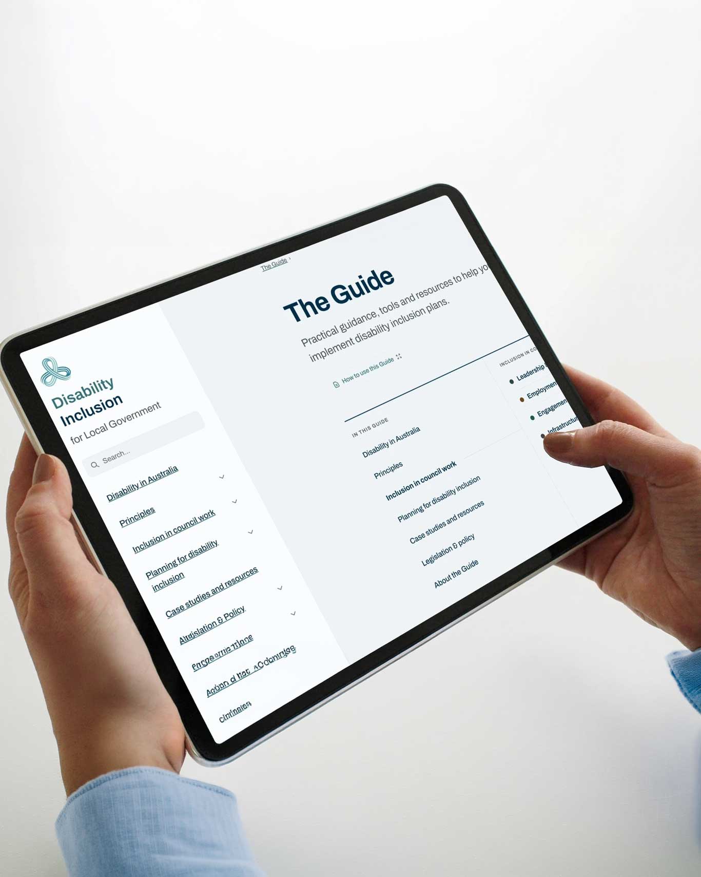 A person holds a tablet displaying the "Disability Inclusion for Local Government" guide website, open on "The Guide" page with a navigation menu listing topics including inclusion in council work, planning for disability inclusion, and case studies.A person holds a tablet displaying the "Disability Inclusion for Local Government" guide website, open on "The Guide" page with a navigation menu listing topics including inclusion in council work, planning for disability inclusion, and case studies.