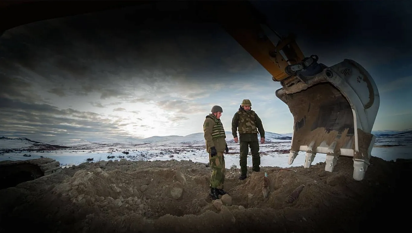 Military personnel inspecting unexploded ordnance with excavator support at Hjerkinn Artillery Range UXO project