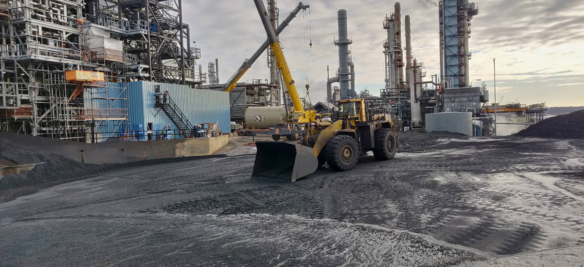 Remote-controlled wheel loader working at industrial facility with cranes and processing units