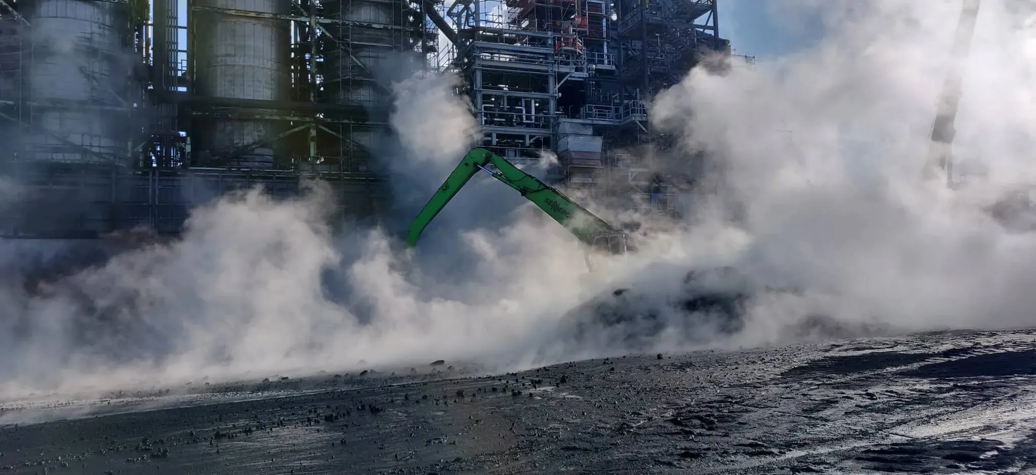 Demolition excavator operating remotely in smoke-filled industrial zone with limited visibility