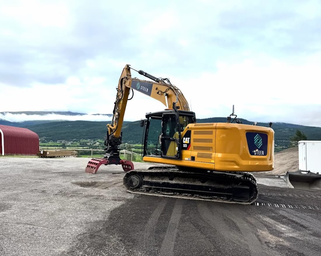 A yellow Caterpillar CAT 323 excavator in teleoperated configuration with a ripper and claw attachment for safe hazard response.