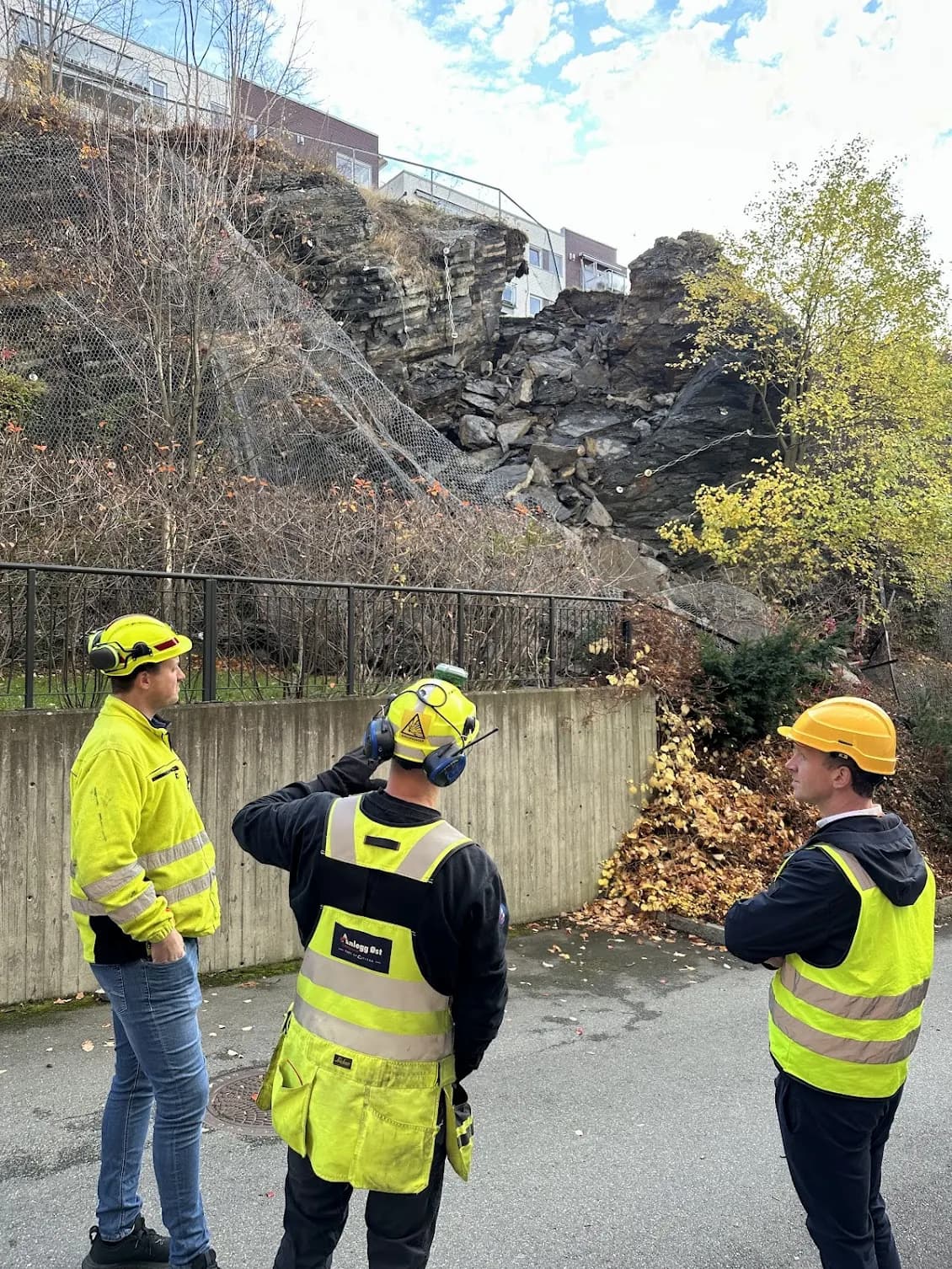 Geologists and engineers inspecting an unstable rock slope with safety netting and fractures after a landslide in an urban area.