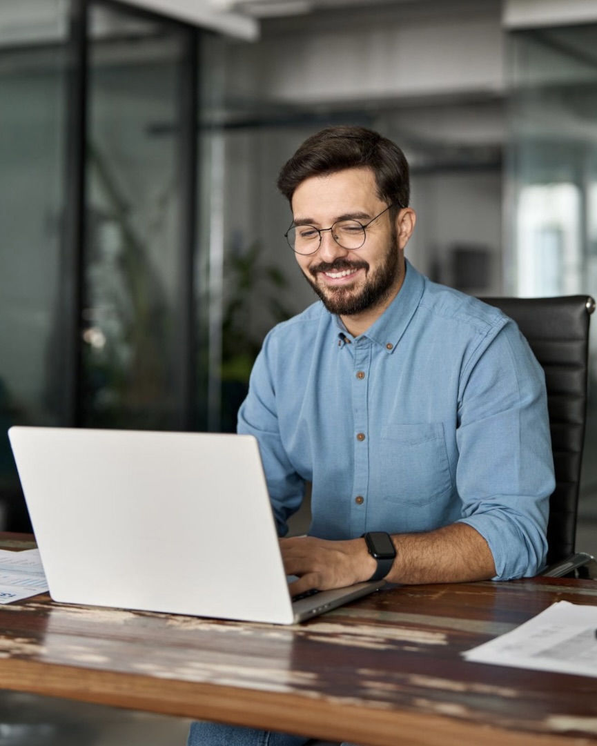 Man smiling while working on a laptop at a desk