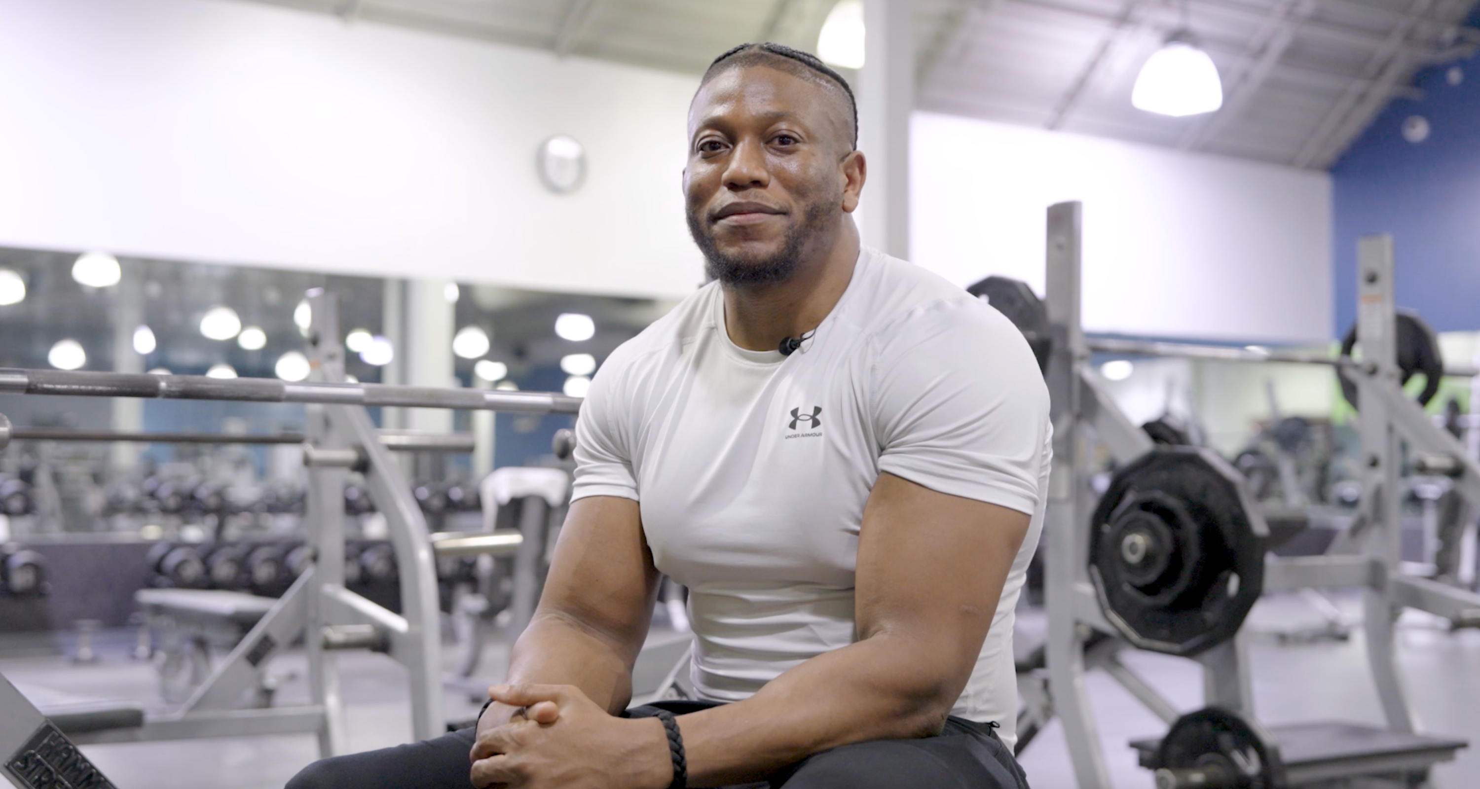 ZIAS sitting confidently on a gym bench with a bench rack behind him, dressed in athletic wear