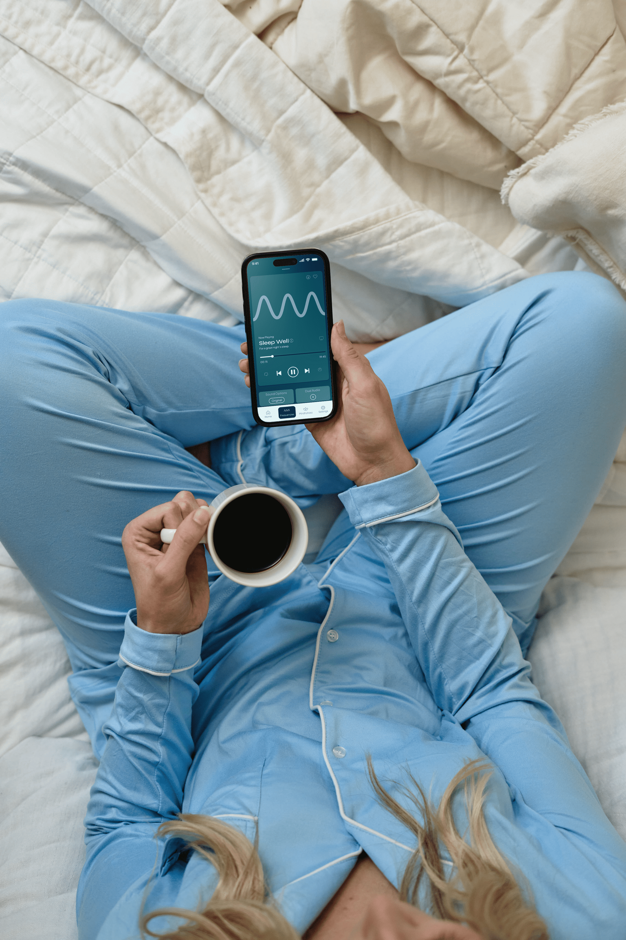 Person holding a mug while a device displays the “Sleep Well” frequency playback.