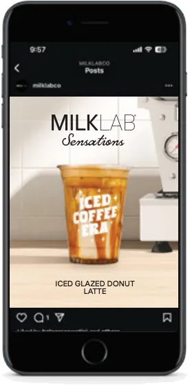 Smartphone screen displaying a social media post from MILKLABCO featuring an iced glazed donut latte in a clear cup with coffee and cream swirls on a countertop.