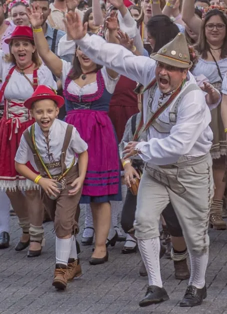 Personnes en costumes traditionnels bavarois dansant et souriant lors d'une fête populaire en plein air.