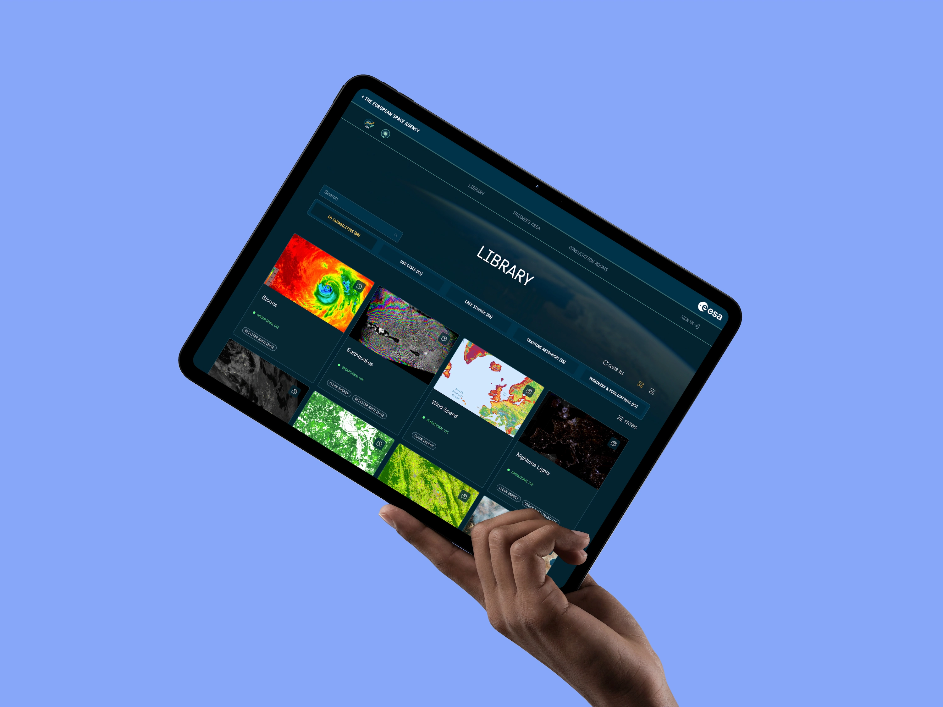 Hand holding tablet displaying European Space Agency library with images on storms and earthquakes.