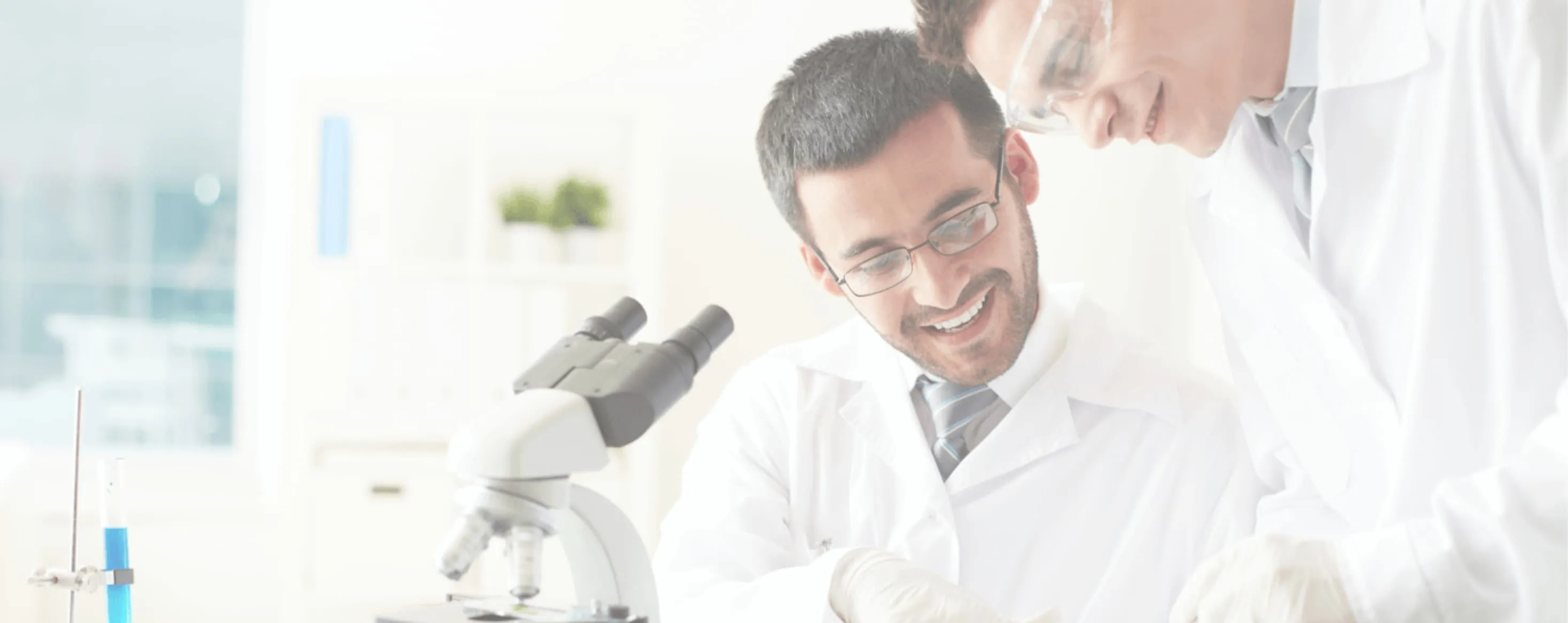 Zwei Männer in weißen Laborkitteln betrachten ein Mikroskop