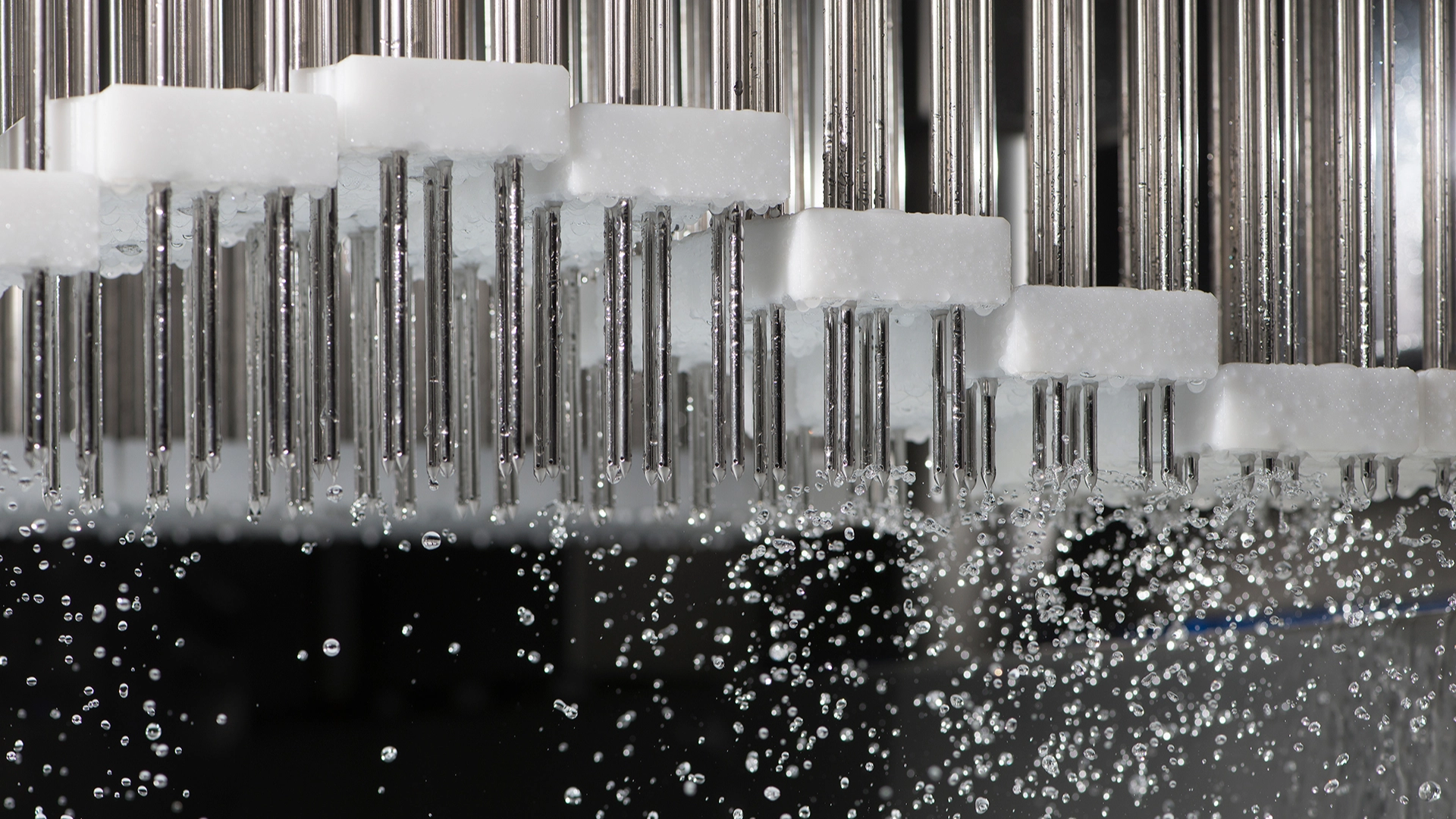 Metal pins with white tops submerged in water with rising bubbles.