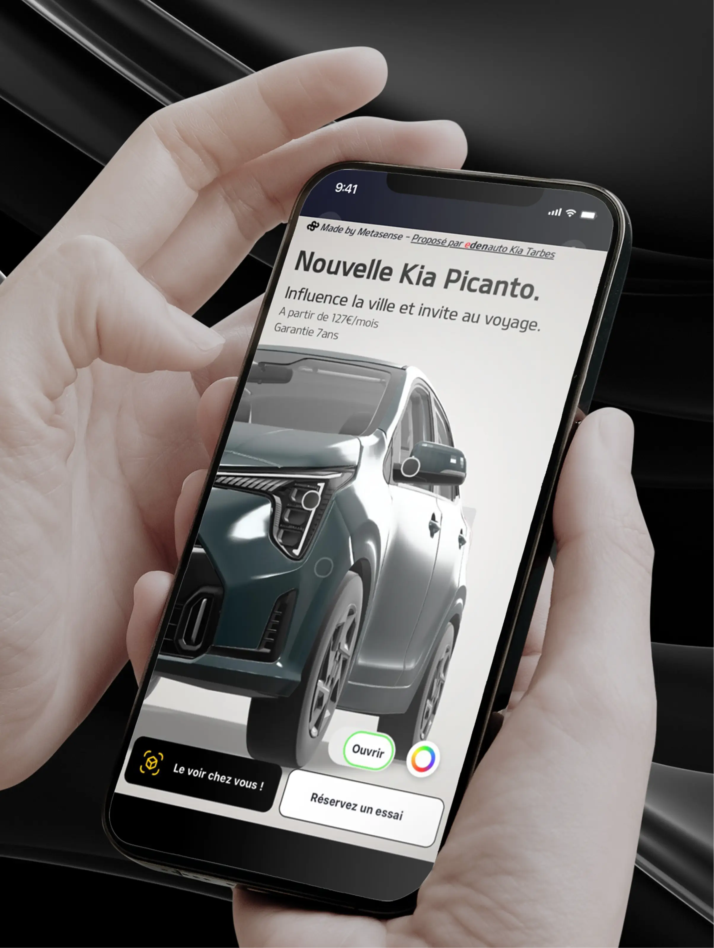Un téléphone tenu en main affichant une publicité pour la Nouvelle Kia Picanto avec une image de la voiture et les options pour la voir chez soi ou réserver un essai.