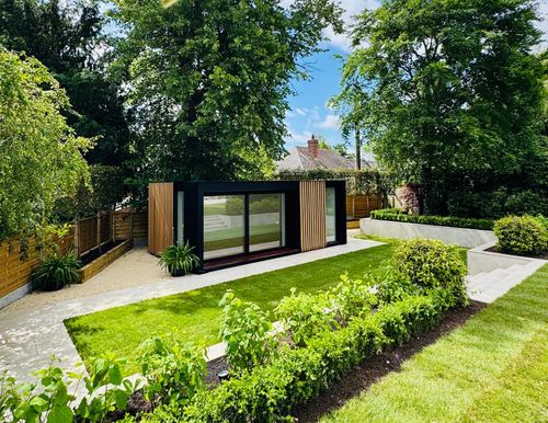 Contemporary sleek black garden building with full height glazing and feature cladding situated within a clean modern landscape design