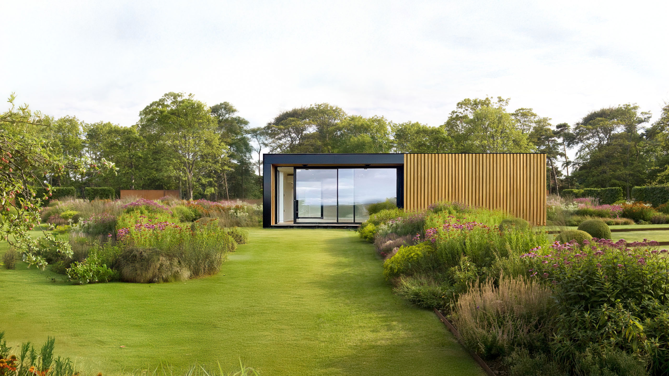 Contemporary garden room with feature natural cladding and full height glazing sits amongst open green lawn and landscaped hedges.