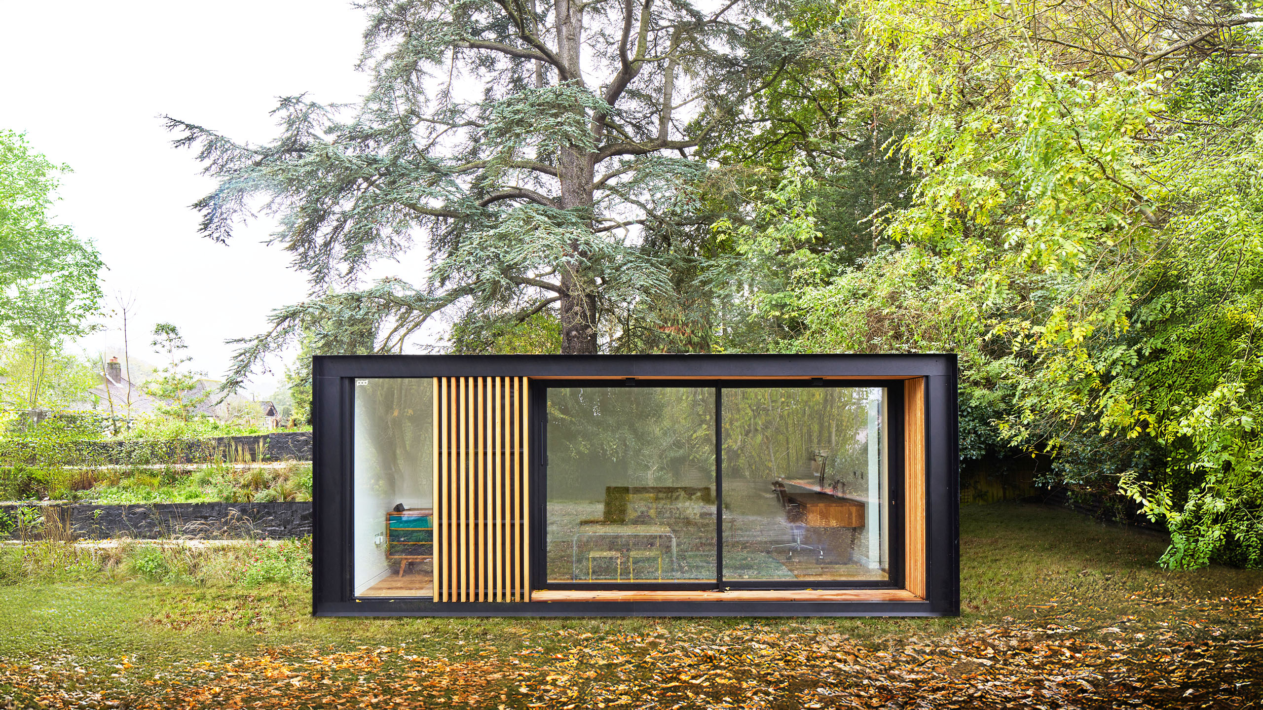 A sleek, modern garden room with large glass windows set among golden autumn leaves and colourful trees.