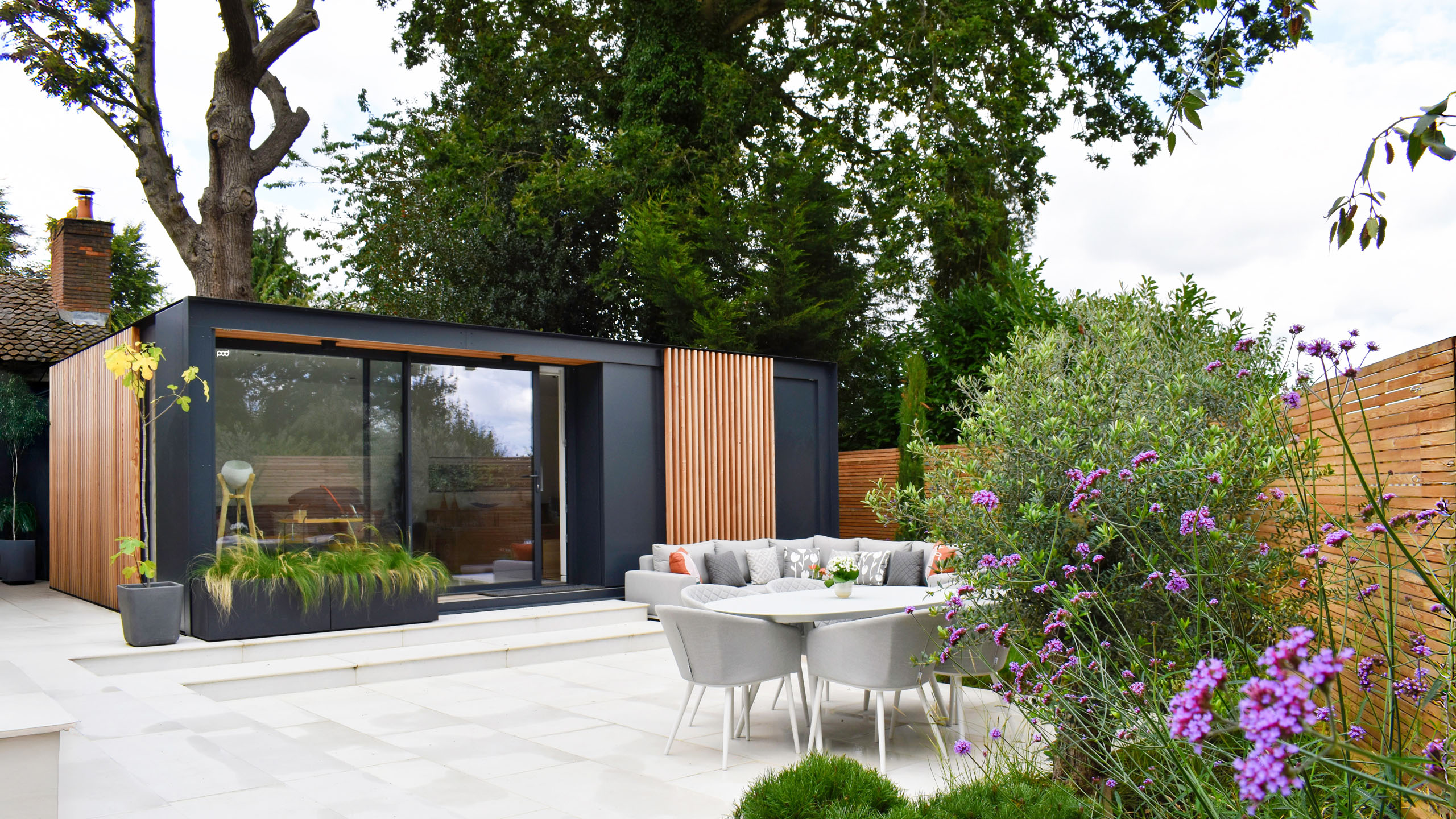 Contemporary garden room with feature wooden cladding and double glass doors surrounded by large grey patio.
