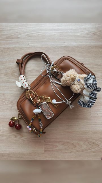 Sac à main marron décoré de charm’s variés, dont une peluche, des cerises, un flacon, une pince à cheveux et des perles colorées.