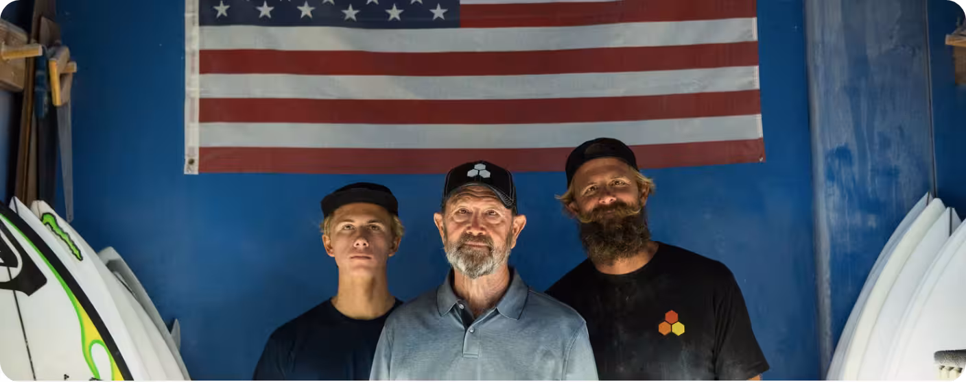 A photo of Al Merrick and Britt Merrick surfboard shapers in front of an American Flag