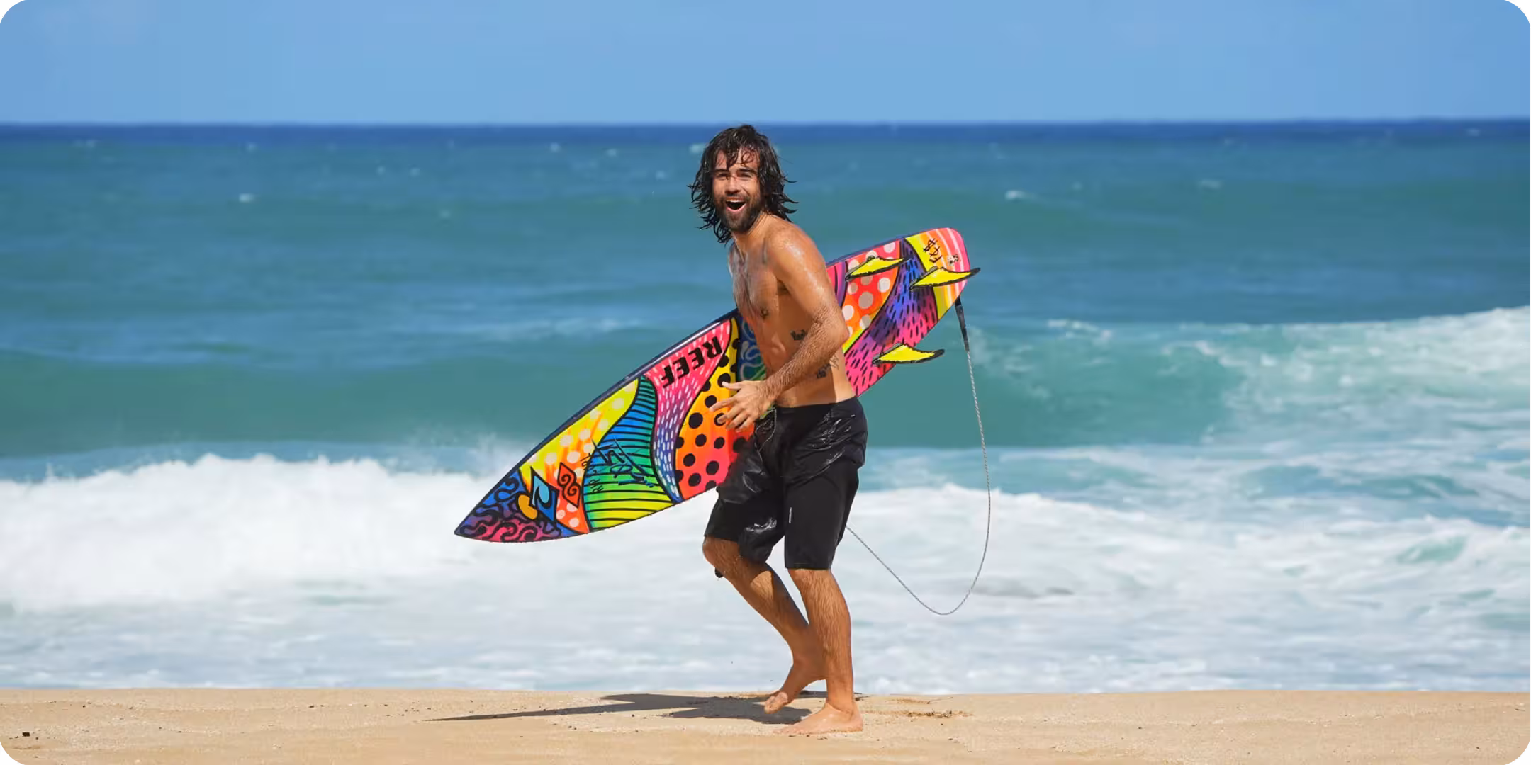 Surfer Mason Ho, walking down the beach with a surfboard
