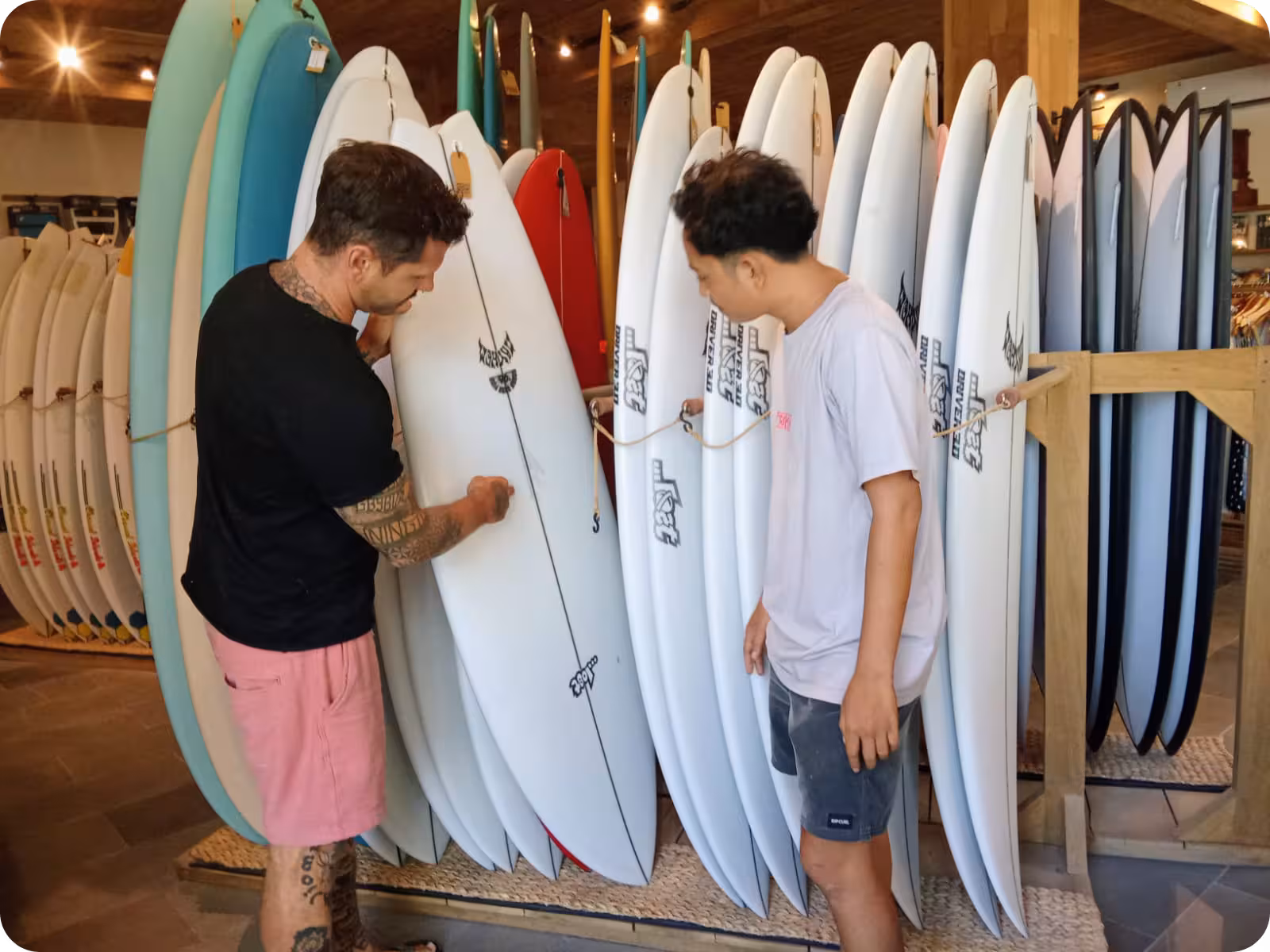 A Flow Surf employee explaining surfboard dimensions to a customer at Flow Surf Lombok surf store