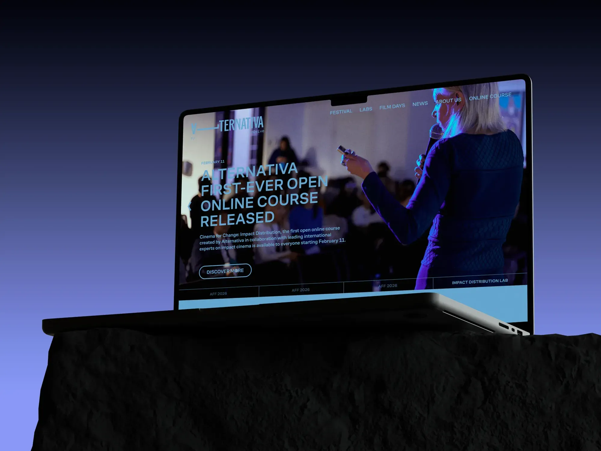 Laptop on a dark rocky surface displays an online course website featuring a woman presenting under blue and purple lighting, creating a futuristic tone.