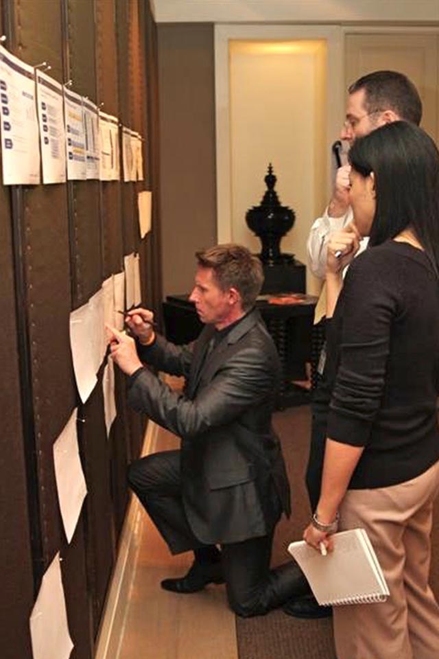 Facilitator kneeling to write on wall charts while a participant looks on, Deutsche Bank project