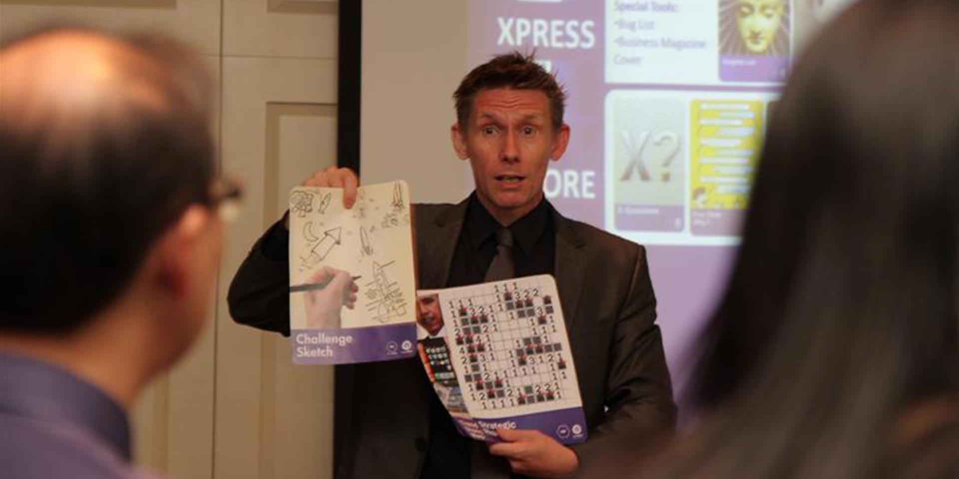 Facilitator holding up X-IDEA challenge sketch cards in front of a projection