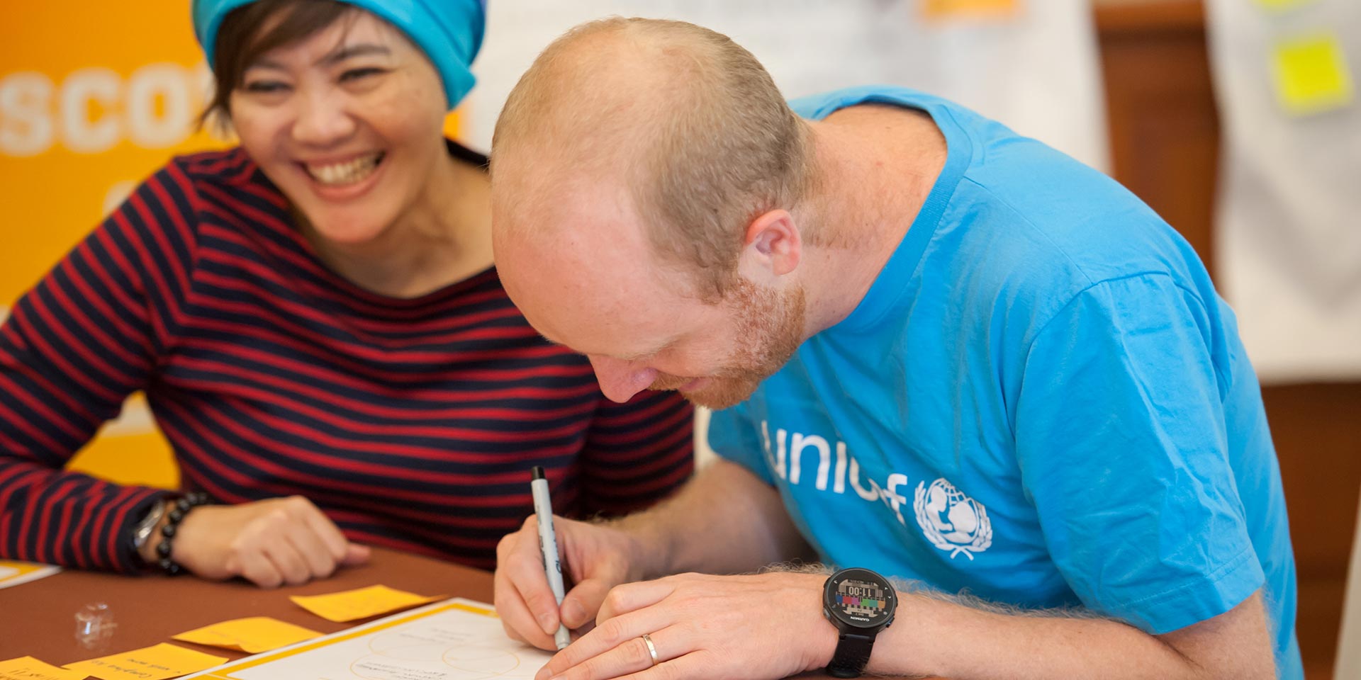 UNICEF staff member writing an idea while a colleague laughs beside him