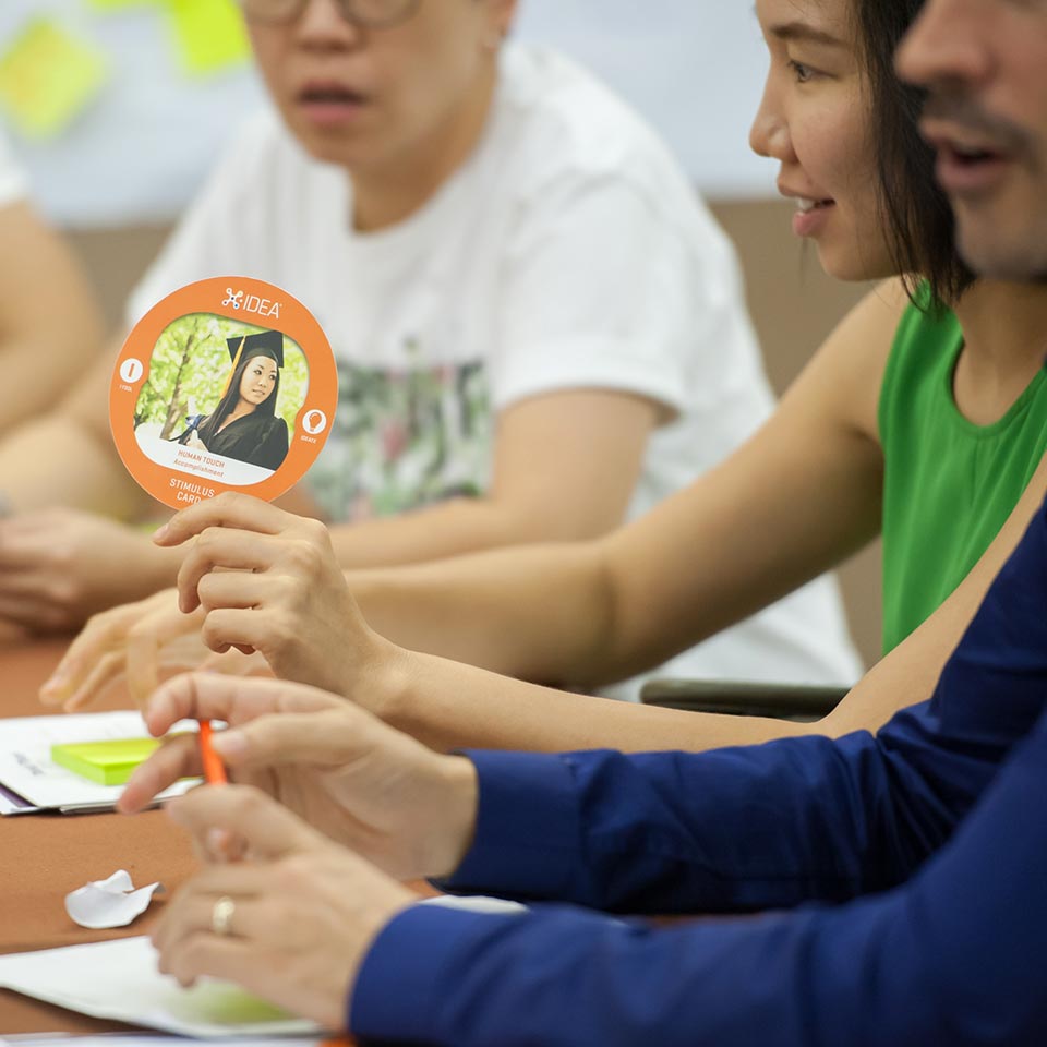 UNICEF participant holding an X-IDEA stimulus card at the workshop table